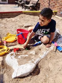 High angle view of boy playing with toys in sandbox on sunny day