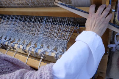 Cropped hand of man weaving wool on loom in factory