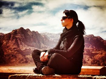 Woman sitting on rock formation against sky at wadi rum
