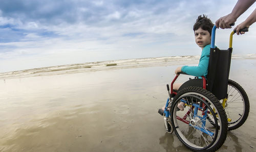 Cropped parent pushing son in wheelchair at beach
