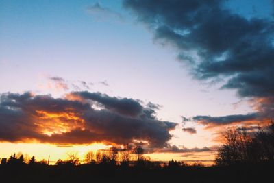 Silhouette trees against dramatic sky during sunset