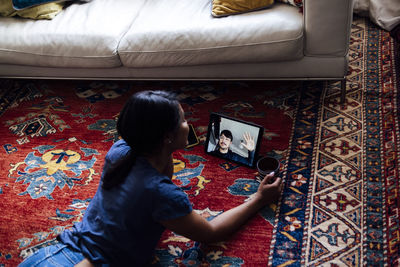 Woman having coffee during video call through digital tablet while lying on on carpet at home