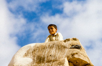 Low angle portrait of smiling man on rock against sky