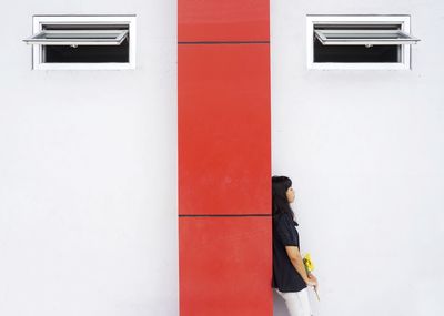 Young woman holding flower while standing against wall