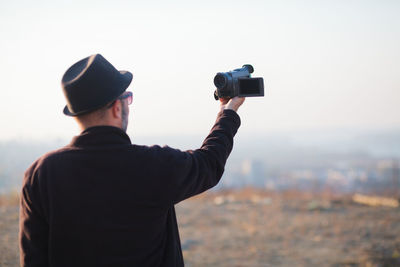 Rear view of man photographing against sky