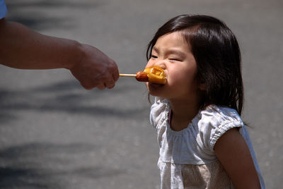 Cropped hand of father feeding bread to daughter on street