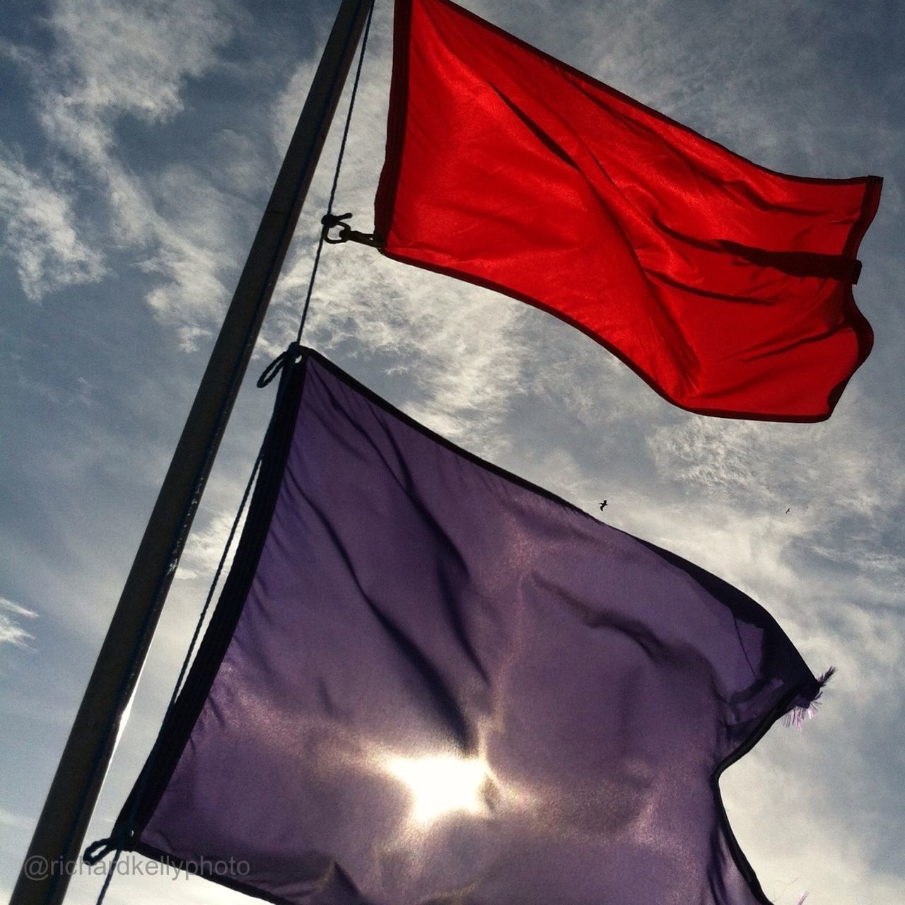 low angle view, flag, sky, patriotism, identity, red, national flag, cloud - sky, american flag, cloud, built structure, cloudy, day, no people, outdoors, sunlight, architecture, wind, building exterior, striped