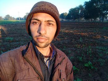 Portrait of young man wearing hat standing against trees