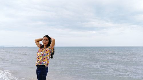 Portrait of woman standing at beach against cloudy sky