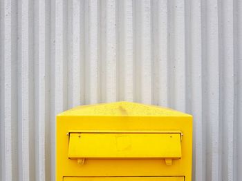Yellow mailbox against corrugated iron
