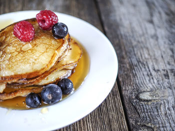 Close-up of pancakes with raspberries and black currants in plate on wooden table