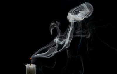 Close-up of candle with smoke over black background