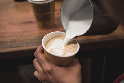 Cropped image of hand pouring milk in coffee