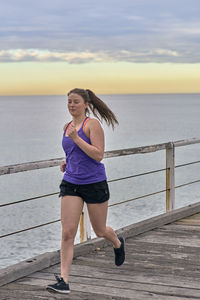 Full length of woman running on boardwalk by sea during sunset