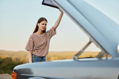 Portrait of young woman standing against car