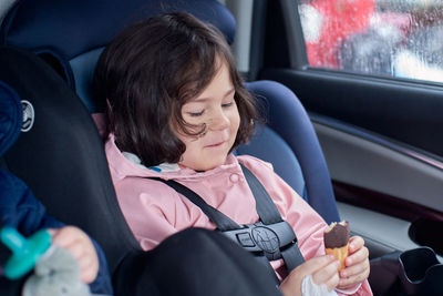 Siblings in car seats having snacks in the back seat of a car on a rainy day