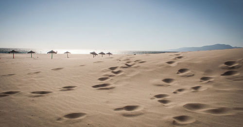 Footprints on sand at beach against clear sky