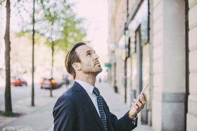 Side view of businessman with phone looking up in city