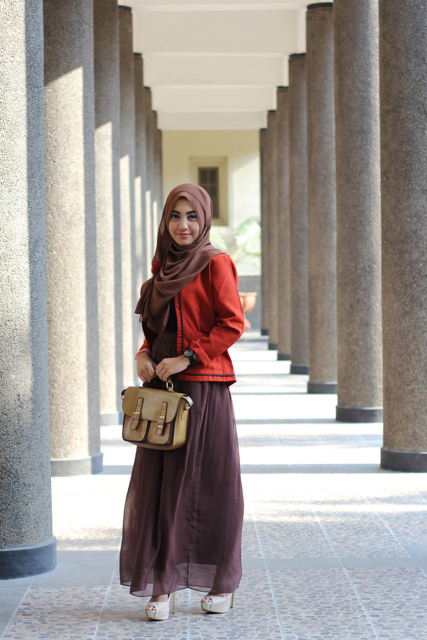 PORTRAIT OF WOMAN STANDING AGAINST WALL