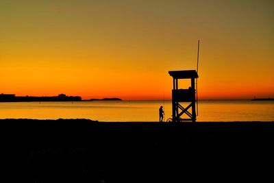 Silhouette lifeguard hut on sea against sky during sunset