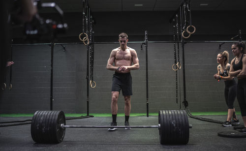 Female athletes cheering man standing by barbell in gym