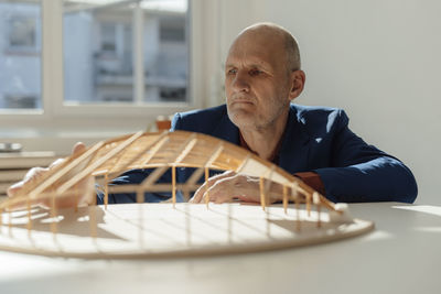 Senior architect analyzing leaf shape wooden model at desk in office