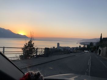 Road by city against sky during sunset