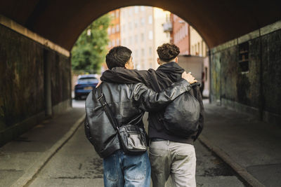 Rear view of teenage male friends walking with arms around through underpass