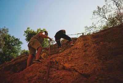 People climbing on rock against sky