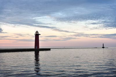 Lighthouse by sea against sky during sunset