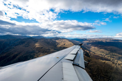 Airplane wing over landscape against sky