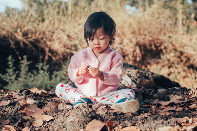 Cute baby girl looking at stone while sitting on land