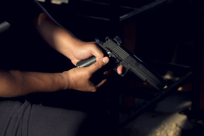 Midsection of man holding handgun while sitting on chair in room