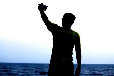 Rear view of silhouette man photographing sea against clear sky