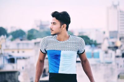 Young man standing in city against sky