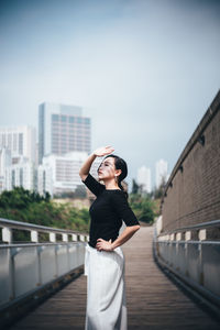 Woman shielding eyes while standing against sky