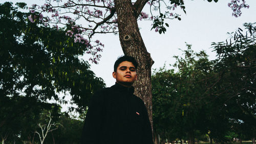 Portrait of young man standing against trees