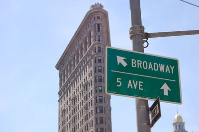 Low angle view of sign board on pole by flatiron building against sky