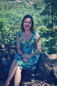 Portrait of woman sitting on rock against trees in forest