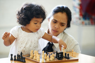 Cute girl playing chess with mother