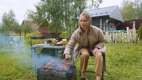 Young man sitting on barbecue grill in yard
