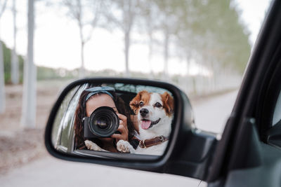 Woman photographing with dog reflecting in car