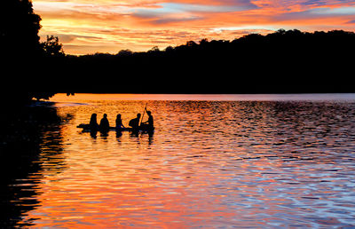 Silhouette of people sitting in rowboat on lake during sunset