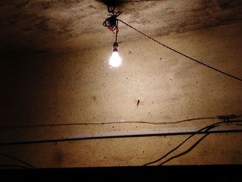 Low angle view of illuminated light bulb hanging against sky