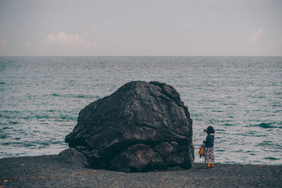 People on rock by sea against sky