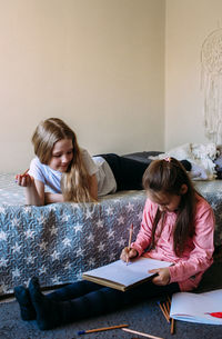 Two girls friends play at home, draw with pencils and felt-tip pens and have fun