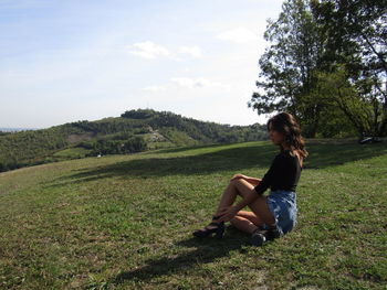 Side view of man sitting on field against sky