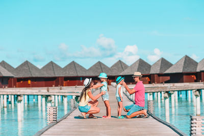 People sitting on pier by swimming pool against sky