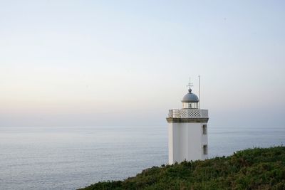 Lighthouse by sea against clear sky