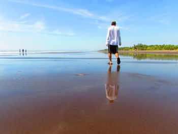 Rear view of man wading in sea against sky